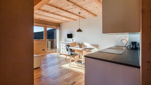 Une cuisine moderne avec des poutres en bois, un coin repas avec une table et des chaises, et une vue sur l’extérieur.