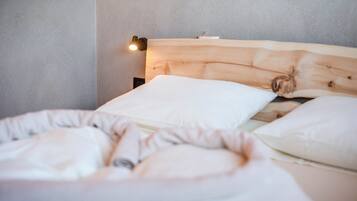 Una cama con cabecera de madera, almohadas blancas y una lámpara fijada a la pared.