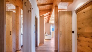 Un couloir au sol et aux portes en bois, qui mène à une pièce où se trouve un canapé blanc.