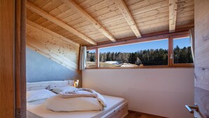 Un plafond en bois, un lit avec une literie blanche et une fenêtre donnant sur des arbres et de la neige.