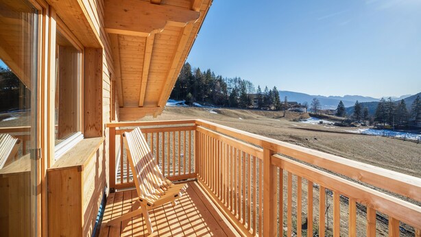 Un balcon en bois offrant une vue sur un paysage enneigé et des montagnes.