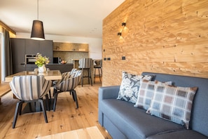 A modern living room with a sofa, striped chairs, a dining table, and a kitchen in the background.