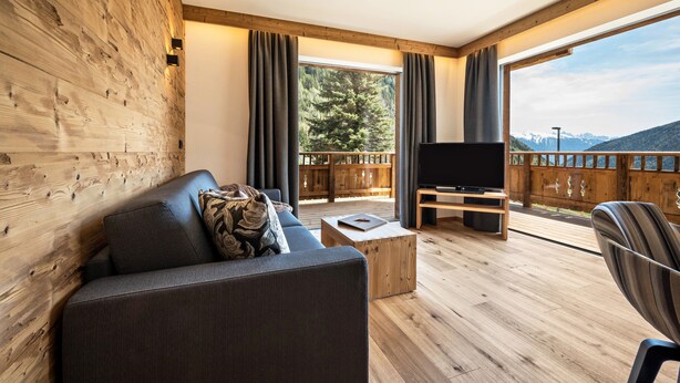 Ein modernes Wohnzimmer mit einer Couch, einem Couchtisch, einem Fernseher und einem Balkon mit Bergblick.
