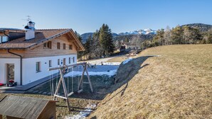 Ein Holzhäuschen mit geneigtem Dach, einer Schaukel und Blick auf schneebedeckte Berge.