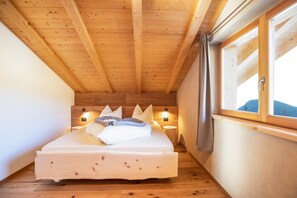 A wooden ceiling, a bed with pillows, a nightstand, a window, and a wall-mounted light.