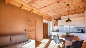 Ein modernes Interieur mit Holzbalkendecke, einer Couch, einem Esstisch mit Stühlen und einer Küchenzeile.