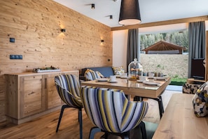 Ein moderner Essbereich mit einer Holzwand, einem Tisch mit Glasplatte, gestreiften Stühlen und Blick ins Freie.