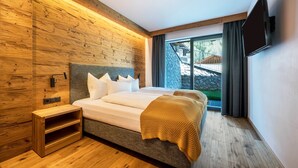Un dormitorio moderno con cabecera de madera, cama con ropa blanca, televisor montado en la pared y una ventana con cortinas.