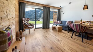Ein Holzinnenraum mit einer Couch, Sesseln, einem Couchtisch und einem Essbereich mit Bergblick.