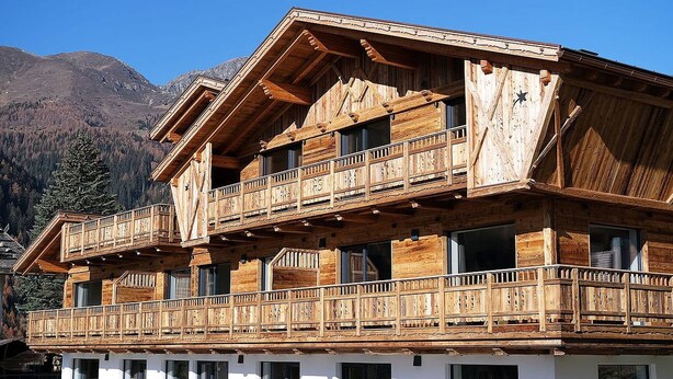 Eine mehrstöckige Holzhütte mit Balkonen vor einer gebirgigen Landschaft.