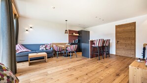 A modern living room with a sofa, a dining table with chairs, a wooden coffee table, and a kitchen area with cabinets and a hanging light. - Apartment "Mulin Loise" next to the Skiing Area with Mountain View, Sauna & Garden (Vals)