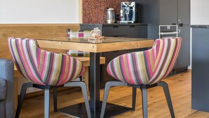 A modern kitchen with a wooden table, two striped chairs, a coffee machine, and a refrigerator. - Apartment "Mulin Loise" next to the Skiing Area with Mountain View, Sauna & Garden (Vals)