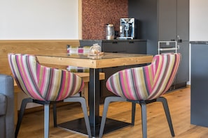 A modern kitchen with a wooden table, two striped chairs, a coffee machine, and a refrigerator.