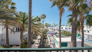A coastal view with palm trees, a narrow street, and white buildings. - Apartamento Sol y Playa with Pool, Wi-Fi, Terrace & Garden (Puerto del Carmen)