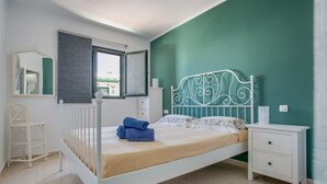 A bedroom with a white bed, a nightstand, a dresser, a window with a view, and a mirror. - Apartamento Sol y Playa with Pool, Wi-Fi, Terrace & Garden (Puerto del Carmen)