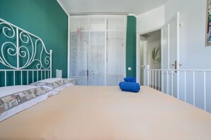 A bedroom with a bed, a white metal headboard, a patterned curtain, and a blue towel on the floor. - Apartamento Sol y Playa with Pool, Wi-Fi, Terrace & Garden (Puerto del Carmen)