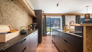 A modern kitchen with wooden flooring, dark cabinetry, and a view of snowy mountains through large windows. - Apartment "Mulin Hilda" next to the Skiing Area with Mountain View, Sauna & Garden (Vals)