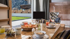 A breakfast table with various food items, a television, and a view of a mountainous landscape. - Apartment "Mulin Hilda" next to the Skiing Area with Mountain View, Sauna & Garden (Vals)