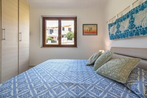A bedroom with a large bed, a window with a view, and a wall with a patterned tapestry. - Apartment 'Isabel' with Shared Pool, Wi-Fi and Air Conditioning (villasimius)