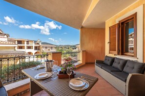 A balcony with a table set for dining, a sofa, and a view of buildings and hills.
