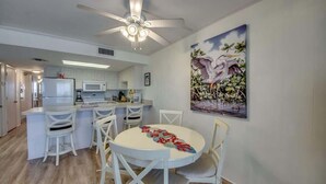 A modern kitchen with white cabinets, a microwave, and a dining area with white chairs and a round table. - Gateway Villas #795 Cozy Beachfront Condo (Fort Myers Beach)