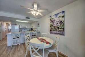 A modern kitchen with white cabinets, a microwave, and a dining area with white chairs and a round table.