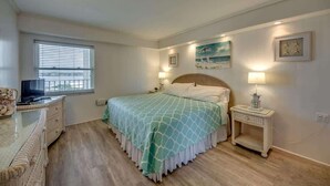 A bedroom with a bed, bedside tables, a TV, and a window with blinds. - Gateway Villas #795 Cozy Beachfront Condo (Fort Myers Beach)