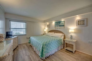 A bedroom with a bed, bedside tables, a TV, and a window with blinds.
