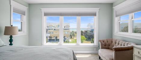 Un dormitorio con cama, una silla, una mesita de noche y una ventana con vistas a casas.