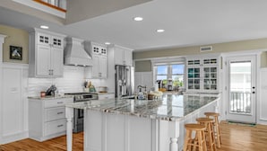 A spacious kitchen with white cabinetry, a large island with stools, and a view to the outside. - "It Was A Good Day" - 2nd Row Home, 4 Bedrooms / 4.5 Bathrooms (Holden Beach)