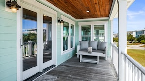 A covered porch with a wooden ceiling, light blue walls, and a white bench with cushions. - "It Was A Good Day" - 2nd Row Home, 4 Bedrooms / 4.5 Bathrooms (Holden Beach)