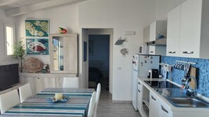 Een moderne keuken met witte kastjes, een blauwe tegelwand en een eethoek met een geruite tafelkleed.