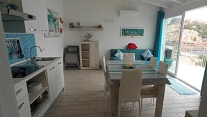 Een compacte keuken met een eethoek, een klein kastje en uitzicht op een heuvel door een groot raam.