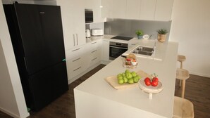 A modern kitchen with white cabinetry, a black refrigerator, and a central island with fresh produce. - Spinnaker Unit 201 (Forster)