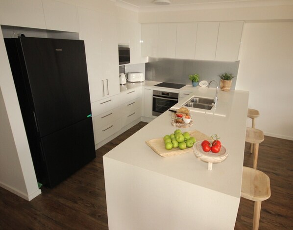A modern kitchen with white cabinetry, a black refrigerator, and a central island with fresh produce.
