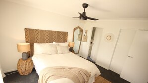 A bedroom with a bed, bedside lamps, a ceiling fan, a mirror, and a door. - Spinnaker Unit 201 (Forster)