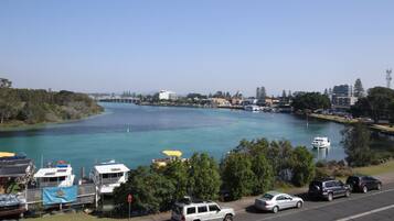 A marina with boats docked, a bridge in the background, and a road with parked cars.