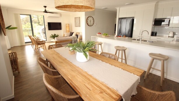A modern kitchen with white cabinets, a wooden dining table, and a hanging light fixture. - Spinnaker Unit 201 (Forster)