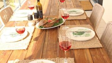A wooden dining table set with plates, cutlery, and wine glasses, surrounded by wicker chairs.