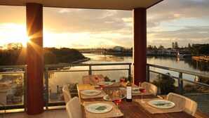 A dining area with a table set for four, overlooking a river and cityscape during sunset. - Spinnaker Unit 201 (Forster)