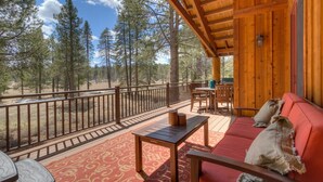 Une terrasse en bois avec un canapé et une table rouges, donnant sur une zone boisée.