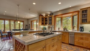 Une cuisine moderne avec des meubles en bois, un grand îlot central et une vue sur l’extérieur grâce à de grandes fenêtres.