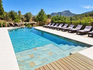 A rectangular swimming pool with clear blue water, surrounded by lounge chairs and a wooden deck.