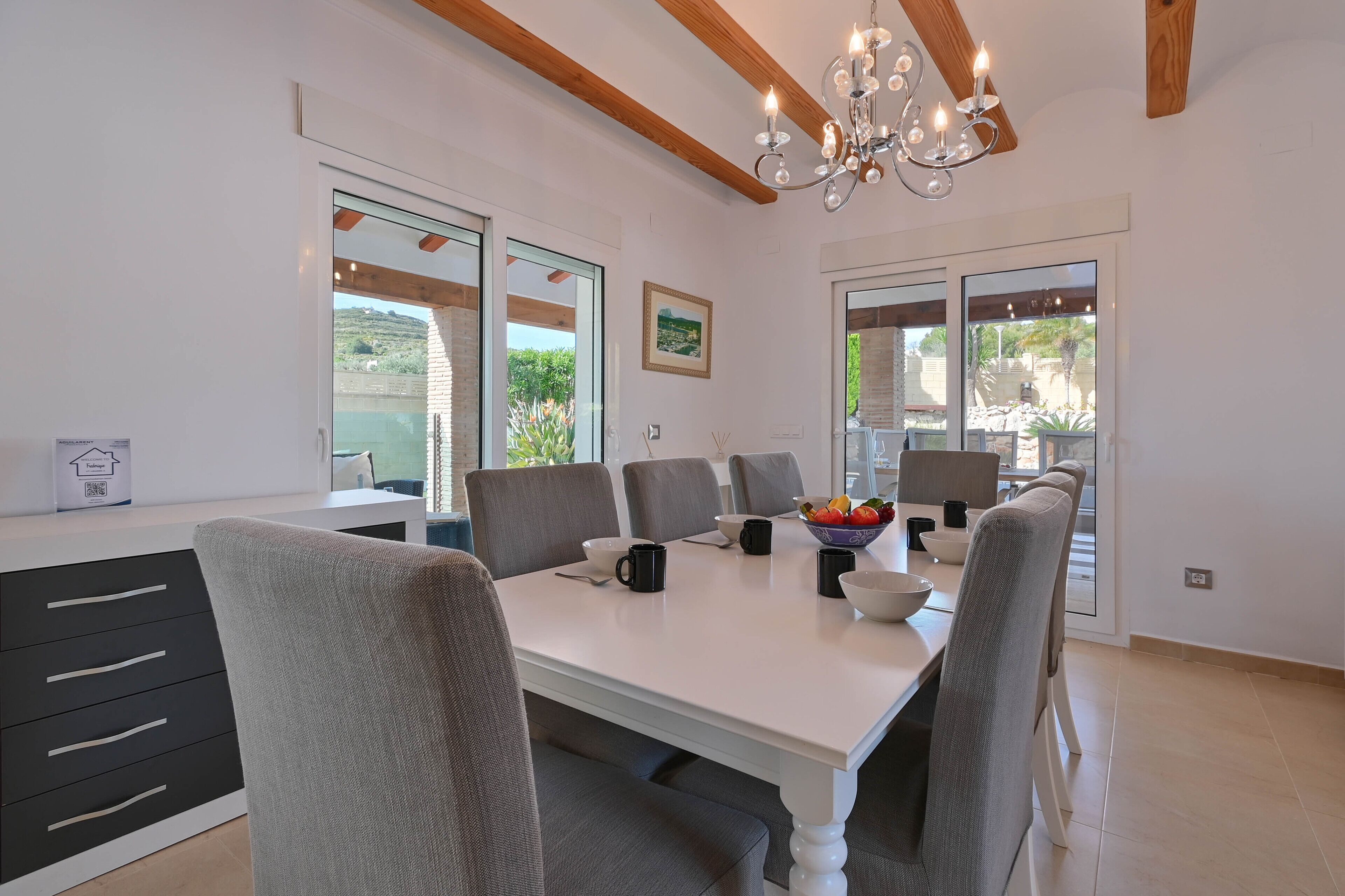 Een moderne eetkamer met een witte tafel, grijze stoelen en een kroonluchter.