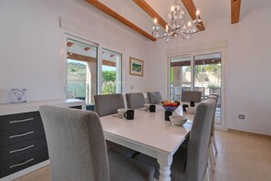 A modern dining room with a white table, grey chairs, and a chandelier.