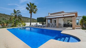 Une piscine à bord incurvé, entourée d’un patio aménagé avec des chaises longues et un espace salon couvert.