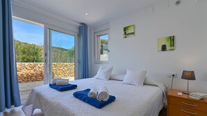 Une chambre d’hôtel avec un grand lit, une table de chevet, une lampe et une vue sur un mur de pierre et la verdure environnante.