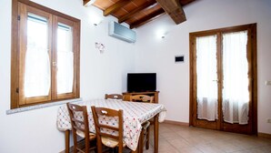 A dining area with a table and chairs, a television, and wooden doors with curtains.