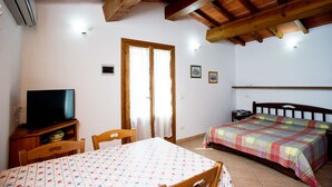 A bedroom with a wooden ceiling, a TV on a wooden cabinet, a bed with a plaid bedspread, and a table with a floral tablecloth.