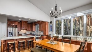 Une cuisine spacieuse avec des meubles en bois, un grand îlot central doté de tabourets, une table à manger avec des chaises et un lustre.